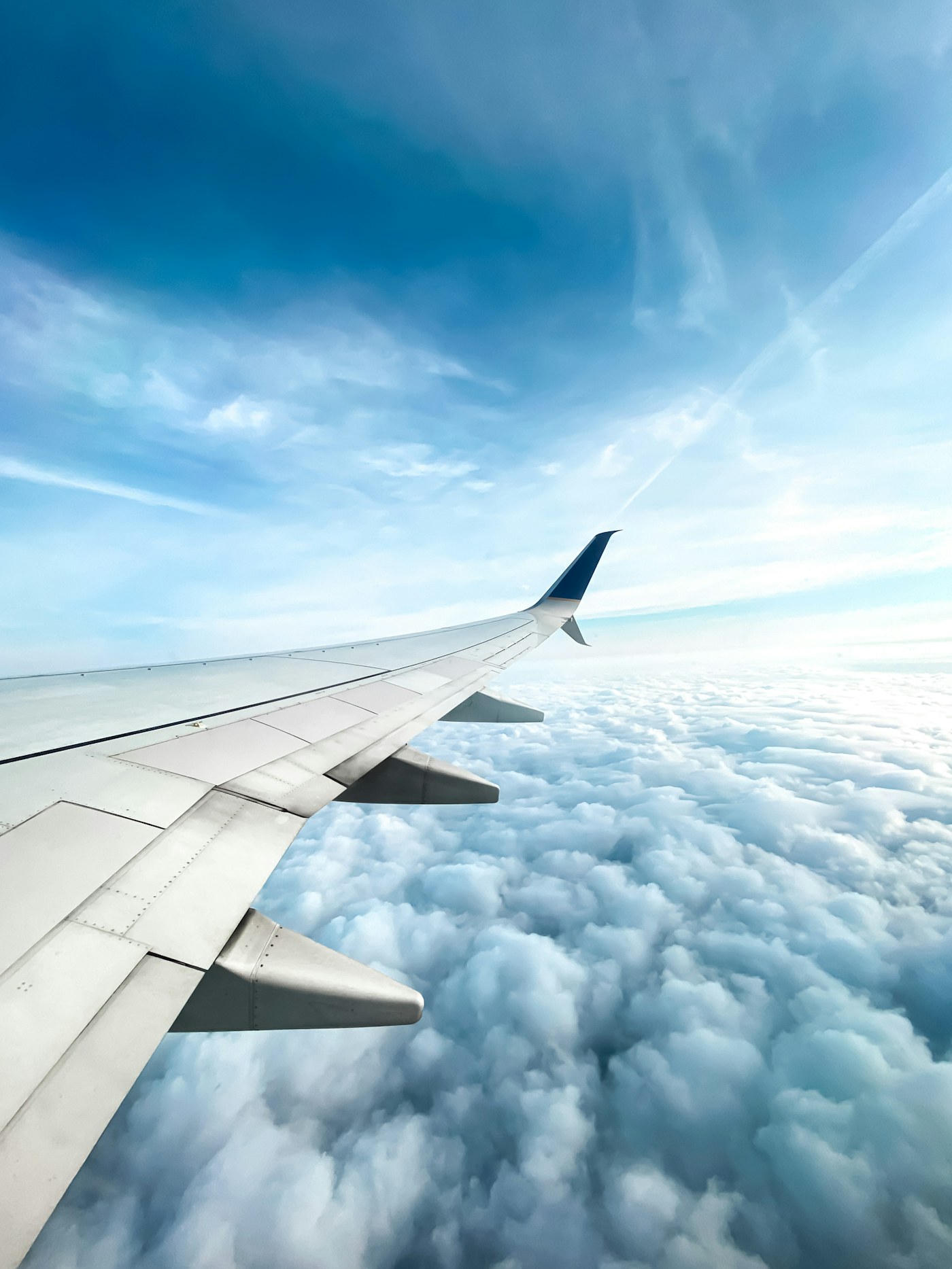 An aircraft wing above white clouds in a blue sky